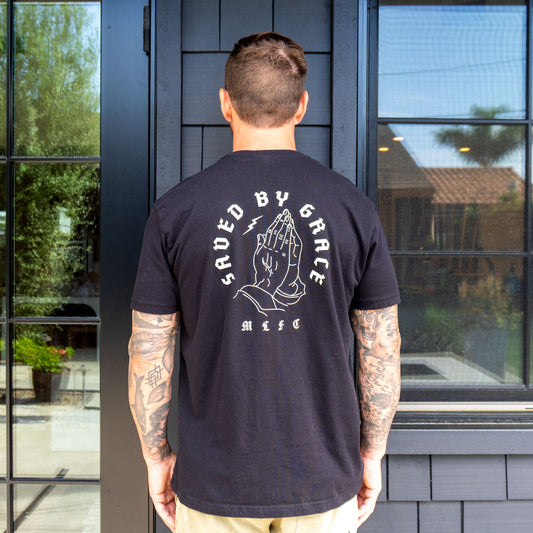 Man wearing black Saved By Grace pocket t-shirt with praying hands graphic on back